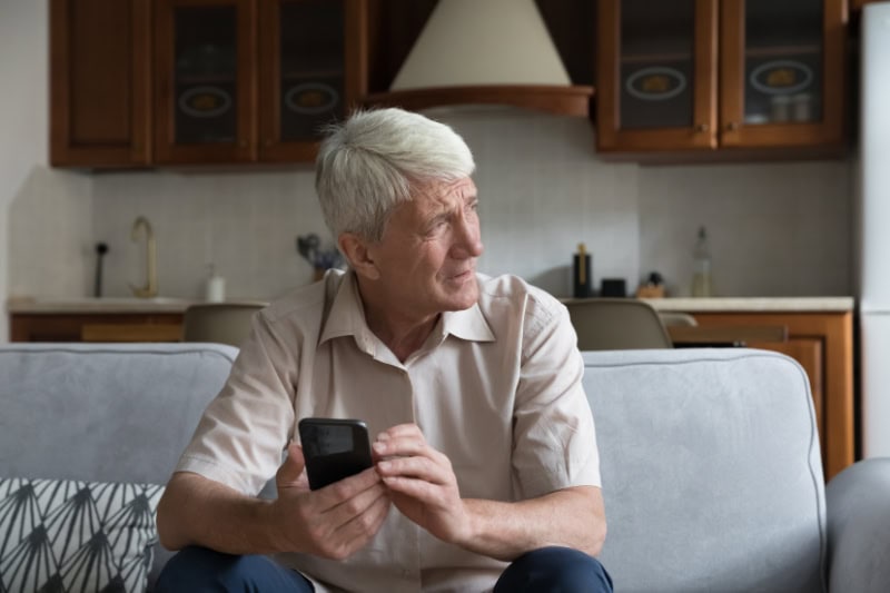 What’s That Smell Coming From My Furnace? Photo of a man on his phone, sitting on his couch and looking out the window, seemingly concerned.
